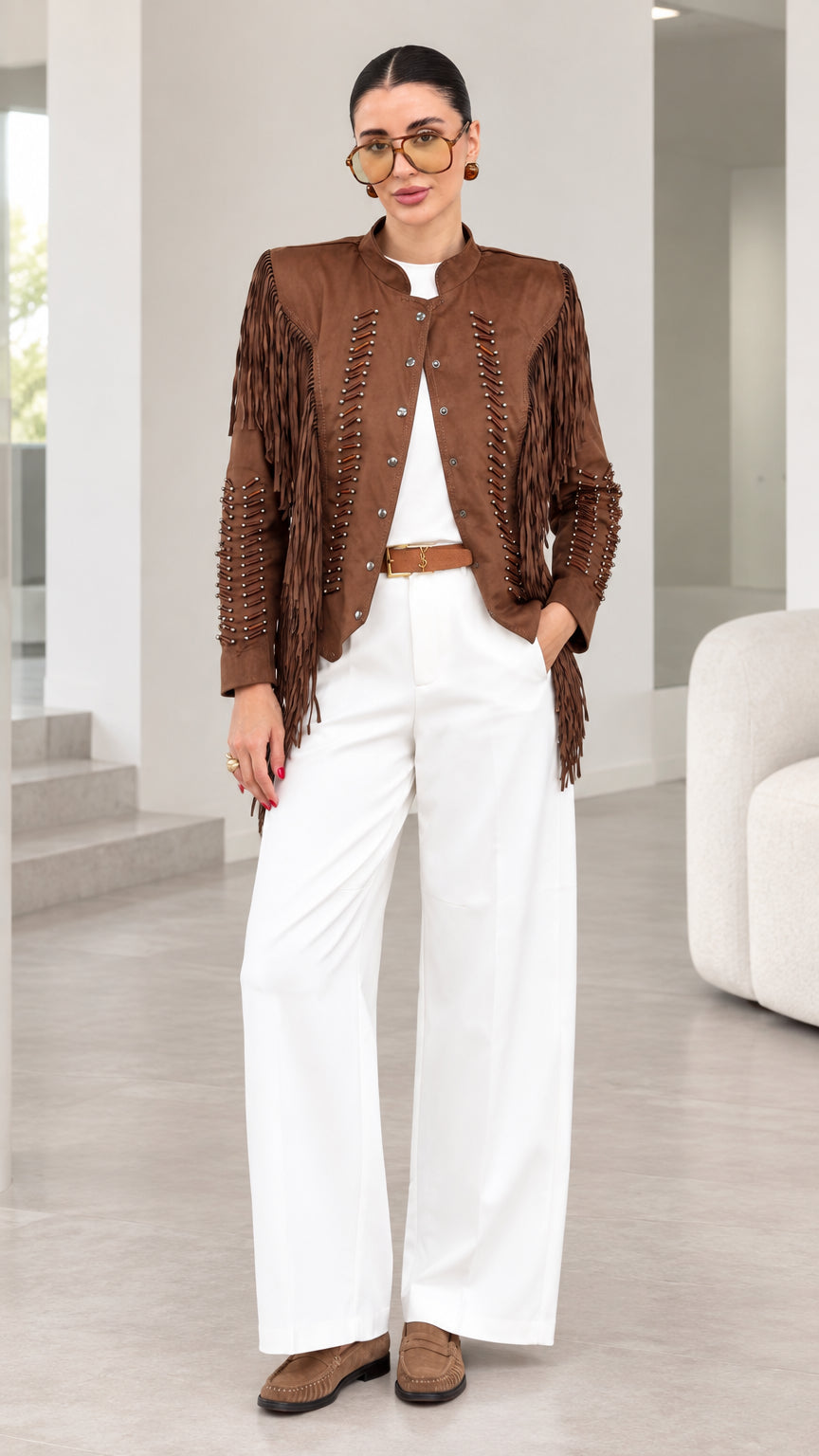 Front full-length view of model wearing brown faux suede fringe jacket with white trousers