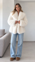 Front view of model wearing ivory plush faux fur lapel coat with light-wash jeans