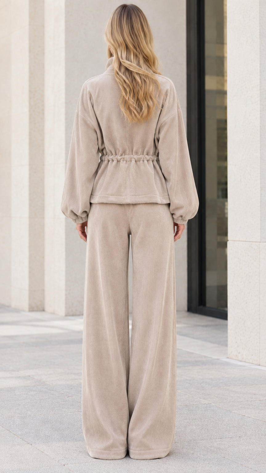Back view of model wearing beige ribbed zip jacket with drawstring waist and wide pants